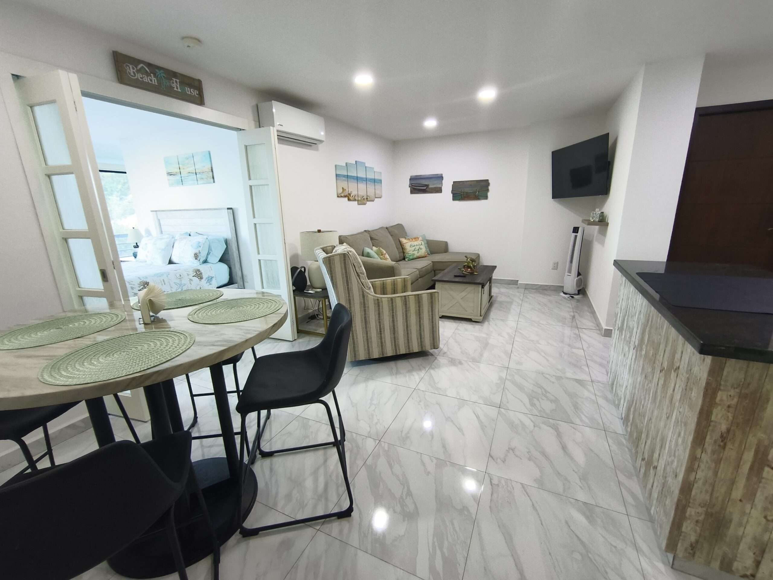 Los Cabos Morgan Residences Morgan Residences Condo 306 offers 67 m² of functional living space with one bedroom, one and a half baths, and a private balcony overlooking the city. The open floor plan connects the kitchen, dining, and living areas with marble-style tile throughout. The kitchen has granite counters, white cabinets, and an island with seating. The bedroom includes an ensuite bathroom with a walk-in shower and opens to the terrace. A separate half bath includes in-unit laundry. The building features a rooftop pool, gym, BBQ area, and for sale
